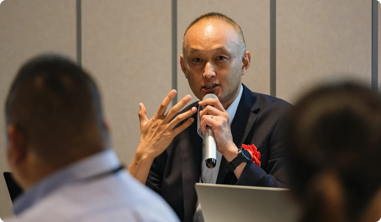 パネルディスカッションの一場面。会津若松市上下水道局 遠藤 利哉氏が、マイクを手に身振りを交えて語っている。胸には受賞者を示す赤いリボン。手前には聴講者の姿。