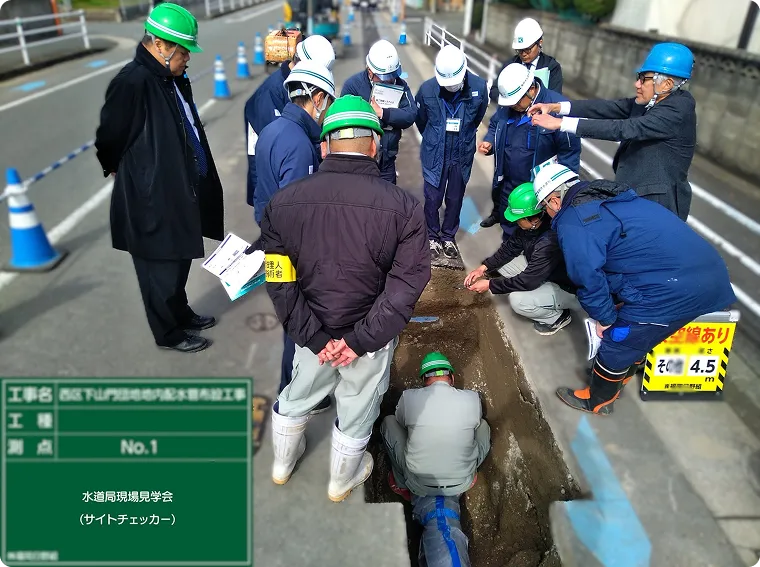発注者を招いた「水道局現場見学会（サイトチェッカー）」で、掘削部の配水管の施工状況を確認する関係者。